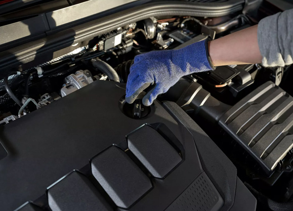 Persona con guantes de taller retirando el tapón de llenado de aceite en el vano motor