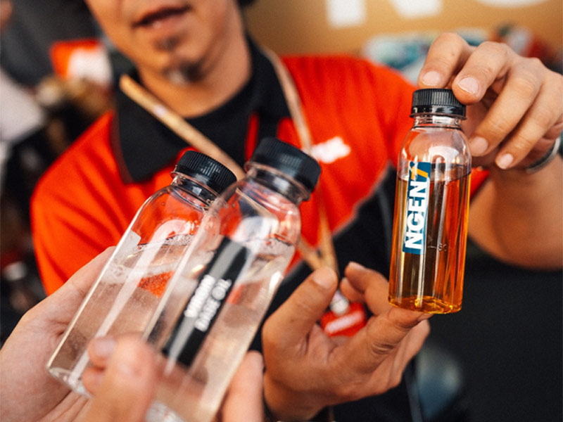 Muestra de aceite Motul Ngen 7 10W40 en recipiente transparente resaltando su color ámbar natural.